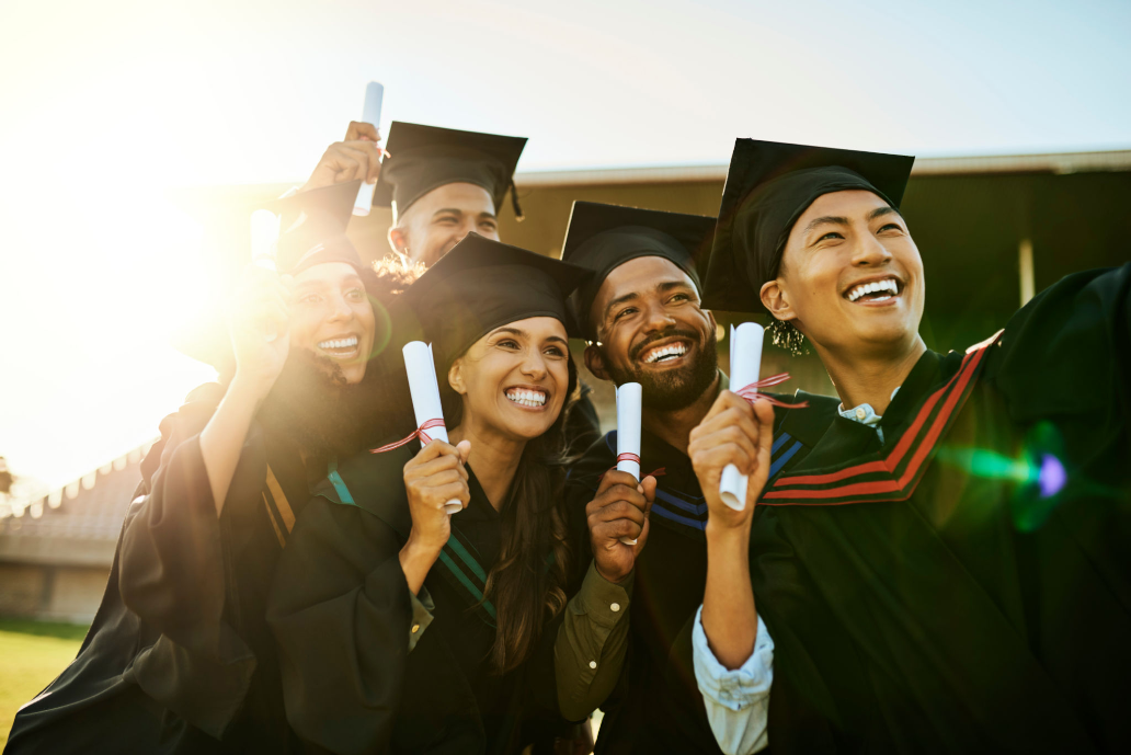 Graduates celebrating with diplomas in sunlight.